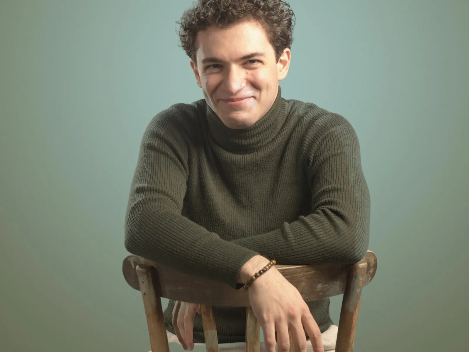 Baritone Biran Özgür Sariyer, studio portrait, leaning on a chair, laughing