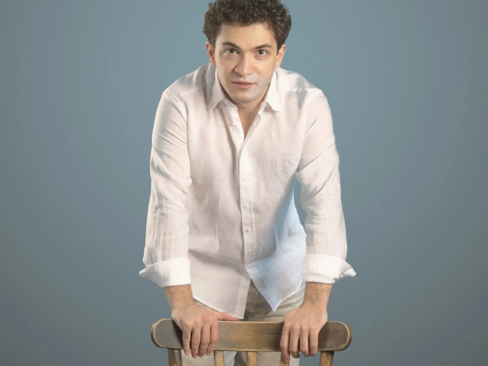 Baritone Biran Özgür Sariyer, studio portrait, leaning on a chair, white linen shirt