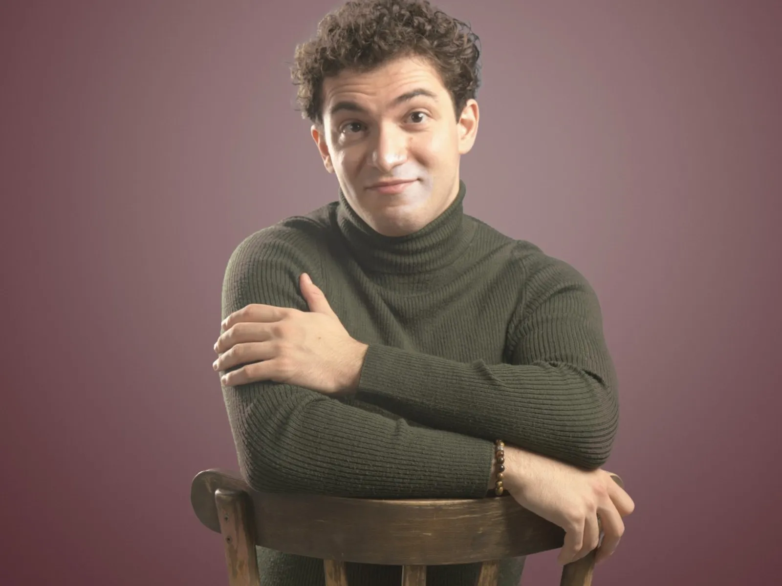 Baritone Biran Özgür Sariyer, studio portrait, leaning on a chair, playful look