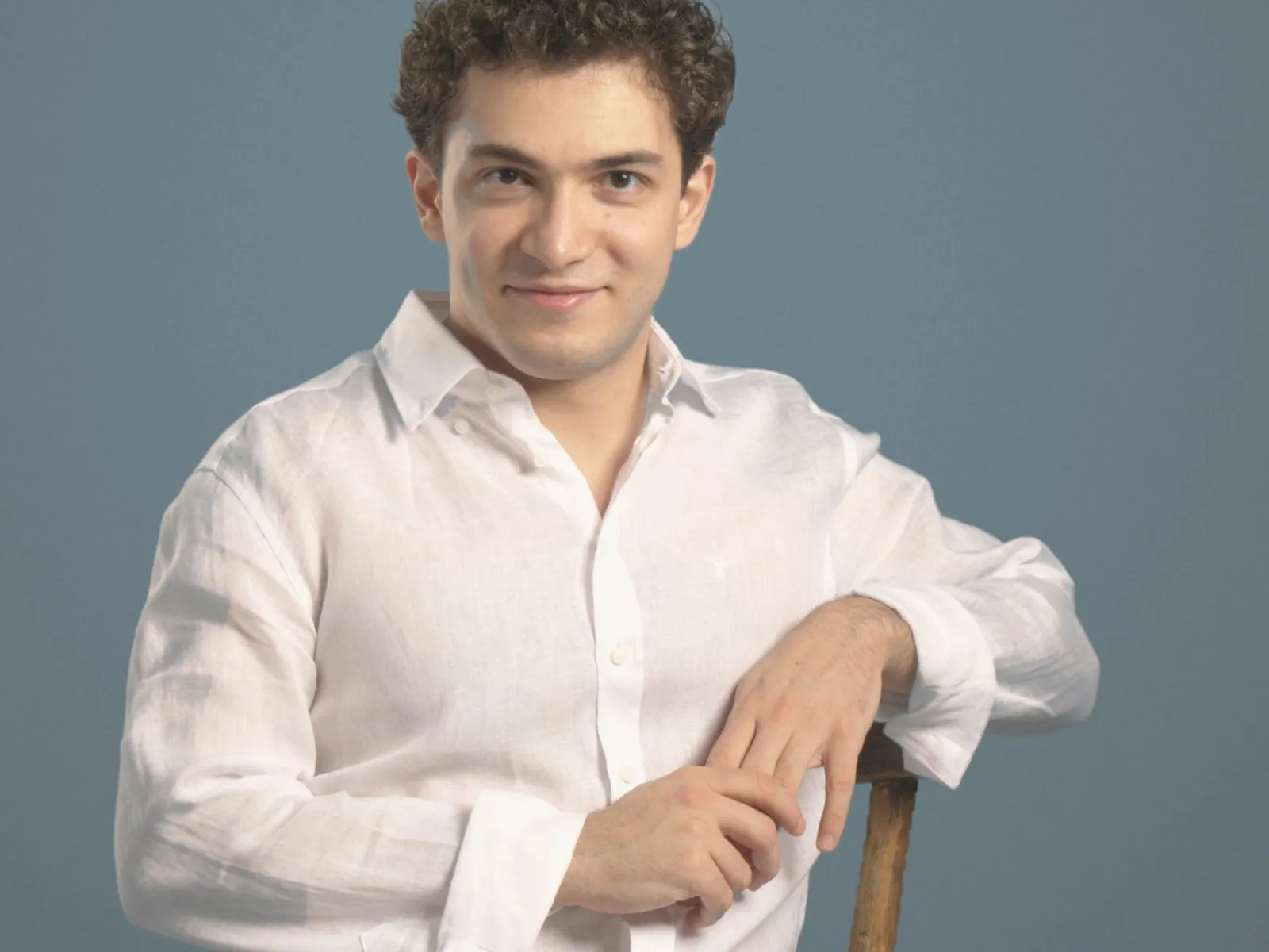 Baritone Biran Özgür Sariyer, studio portrait, seated, white linen shirt, smiling