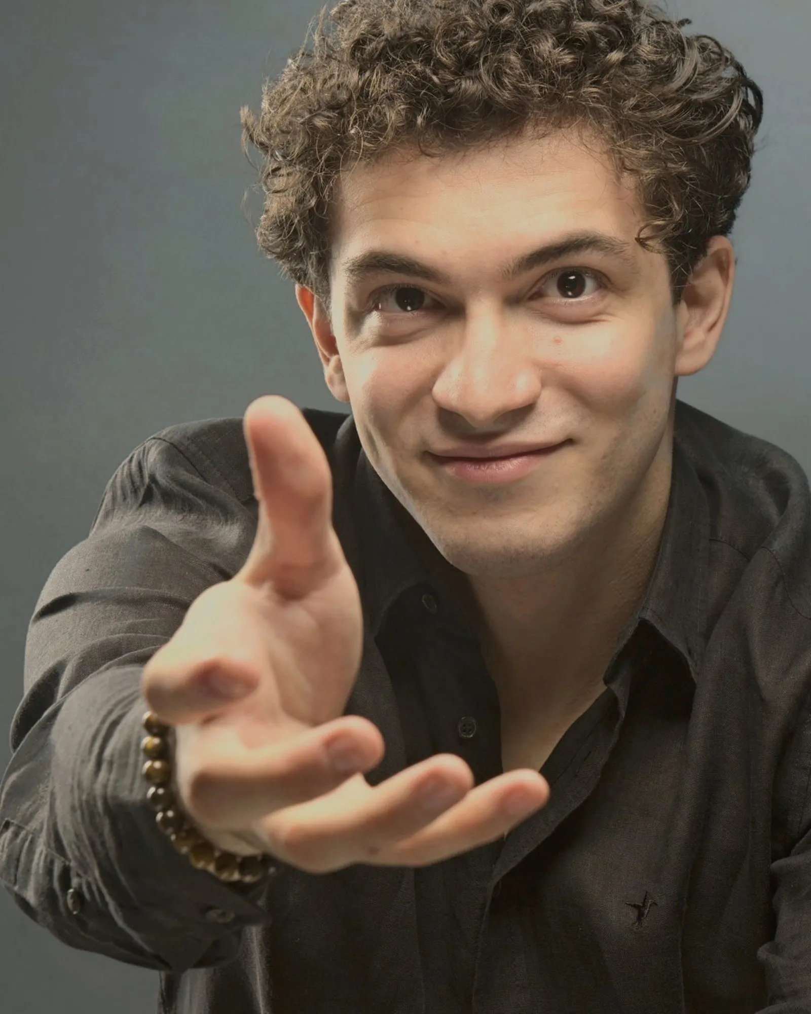 Baritone Biran Özgür Sariyer, studio portrait, reaching out a hand, black shirt